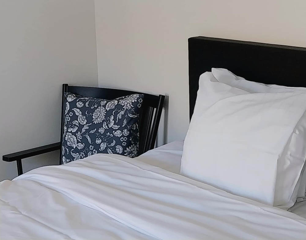 Ljust hotellrum med vit säng och fåtölj vid väggen